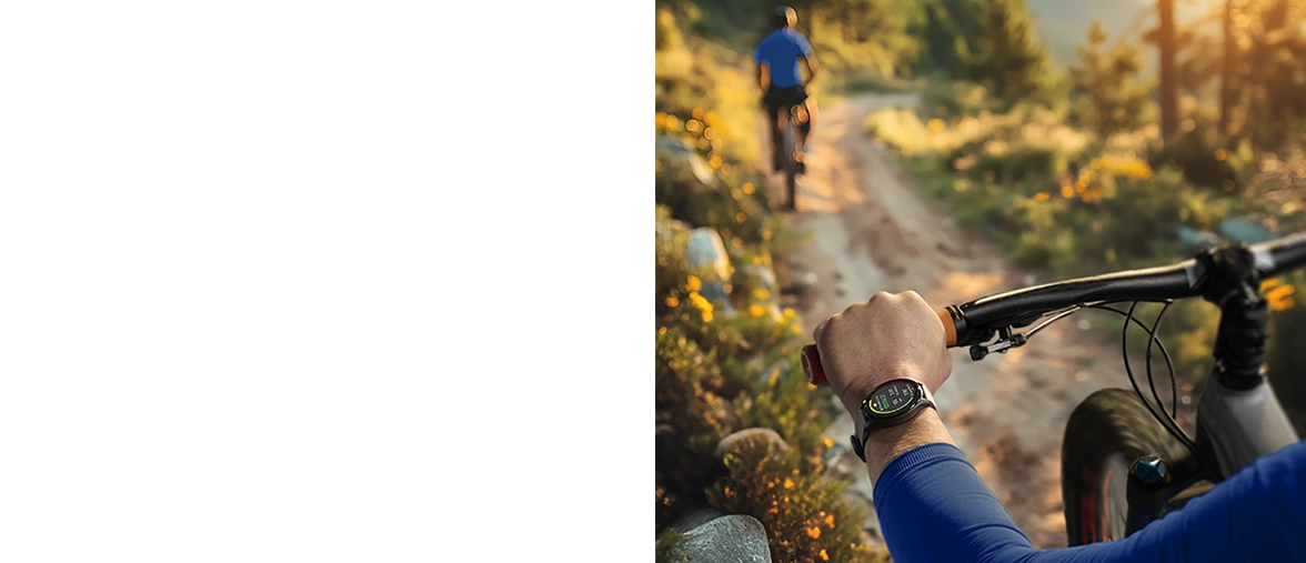 Widok zza ramienia rowerzysty jadącego żwirową drogą otoczoną zielonymi łąkami, noszącego smartwatch Hama na lewym nadgarstku.